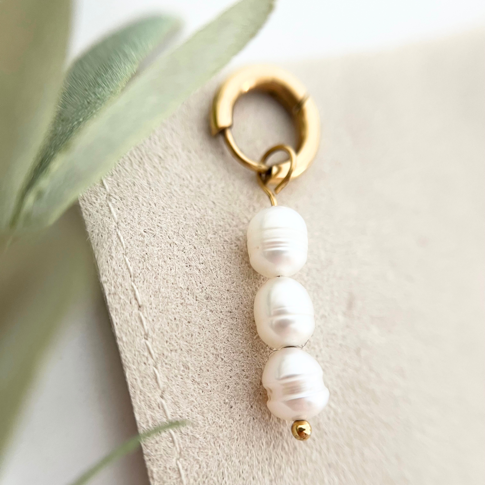 Detailaufnahme eines goldenen Edelstahl-Ohrrings PERLA mit schimmernder weißer Süßwasserperle, die den edlen Charme des Schmuckstücks zeigt.