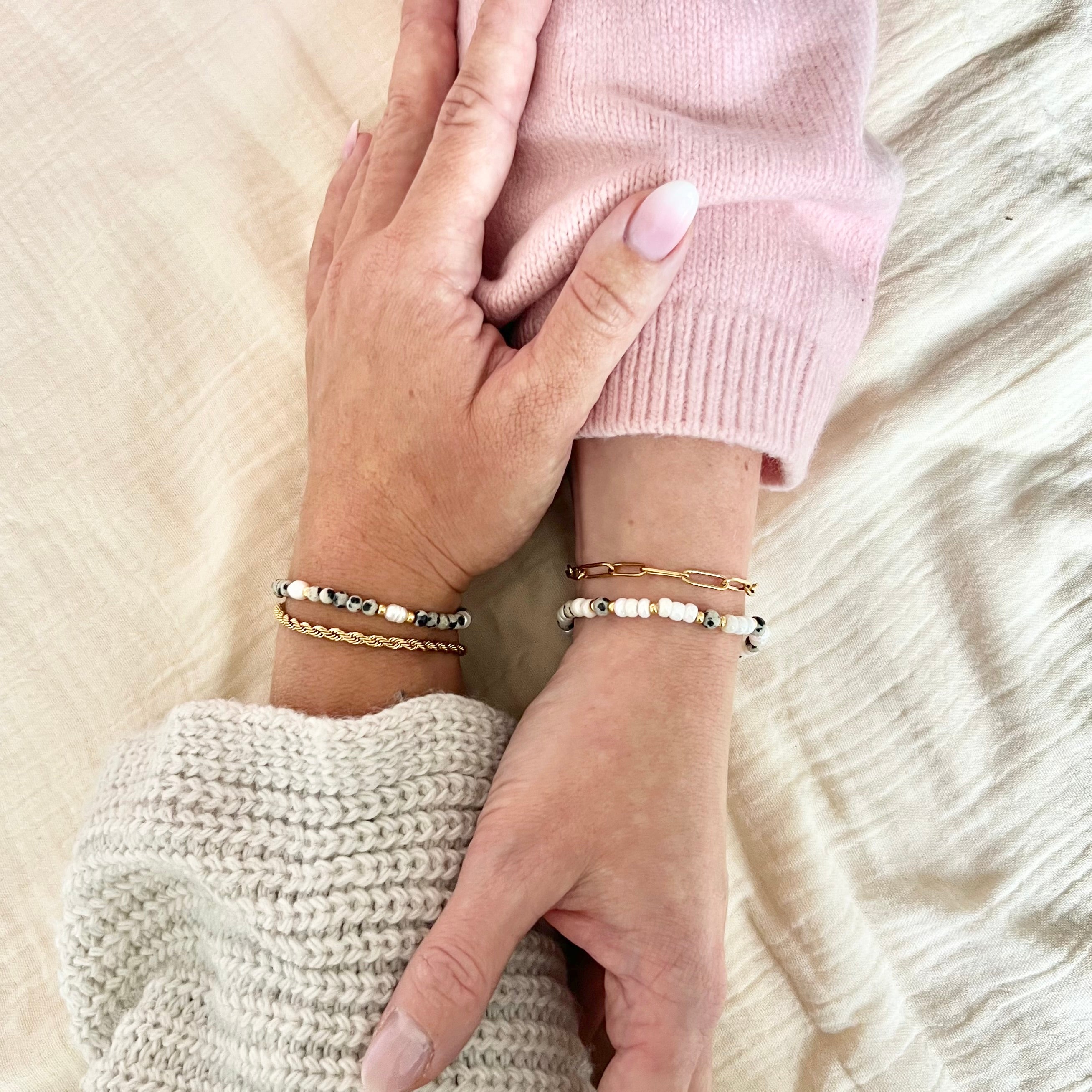 Zwei Hände mit passenden Freundschaftsarmbändern in Naturtönen und Gold, Symbol für Zusammenhalt und Freundschaft, warmer Hintergrund in Beige.
