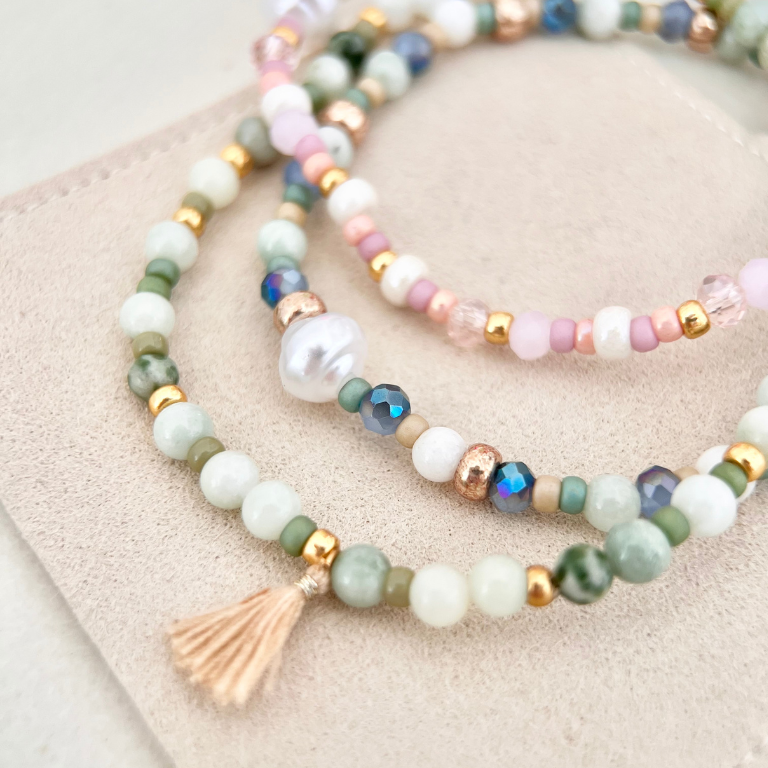 Perlenarmband Set in verschiedenen Farbkombinationen auf beigem Wildlederpad, mit Quaste, bunten und weißen Perlen sowie goldenen Akzenten – DIY Schmuckset zum Armband basteln