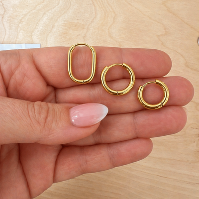 Hand hält drei goldene Edelstahl Creolen in oval und rund, Huggie Hoops Ohrringe für Mix & Match Kombination