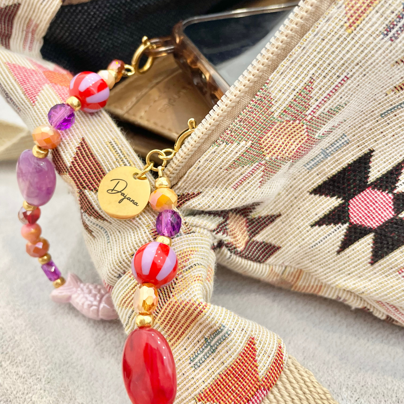 Nahaufnahme einer handgemachten Handykette mit bunten Acryl-, Glas- und Natursteinperlen in Pink-, Orange- und Lilatönen mit goldenen Miyuki-Zwischenperlen – personalisierte Handykette als stylisches Handyband.