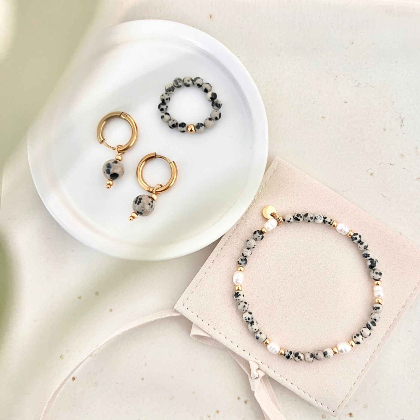 Handgefertigter Perlenring aus Dalmatiner Jaspis Natursteinperlen mit goldfarbener Edelstahlperle, kombiniert mit passenden Ohrringen und Armband, stilvoll präsentiert als alltagstauglicher Schmuck.