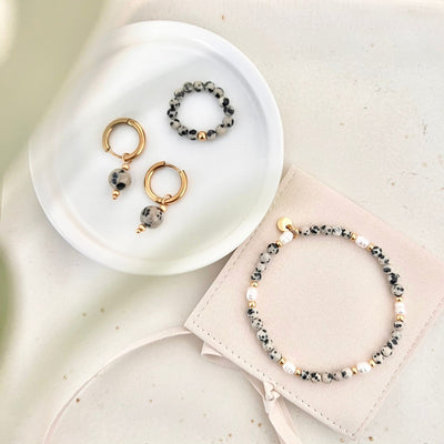 Handgefertigter Perlenring aus Dalmatiner Jaspis Natursteinperlen mit goldfarbener Edelstahlperle, kombiniert mit passenden Ohrringen und Armband, stilvoll präsentiert als alltagstauglicher Schmuck.