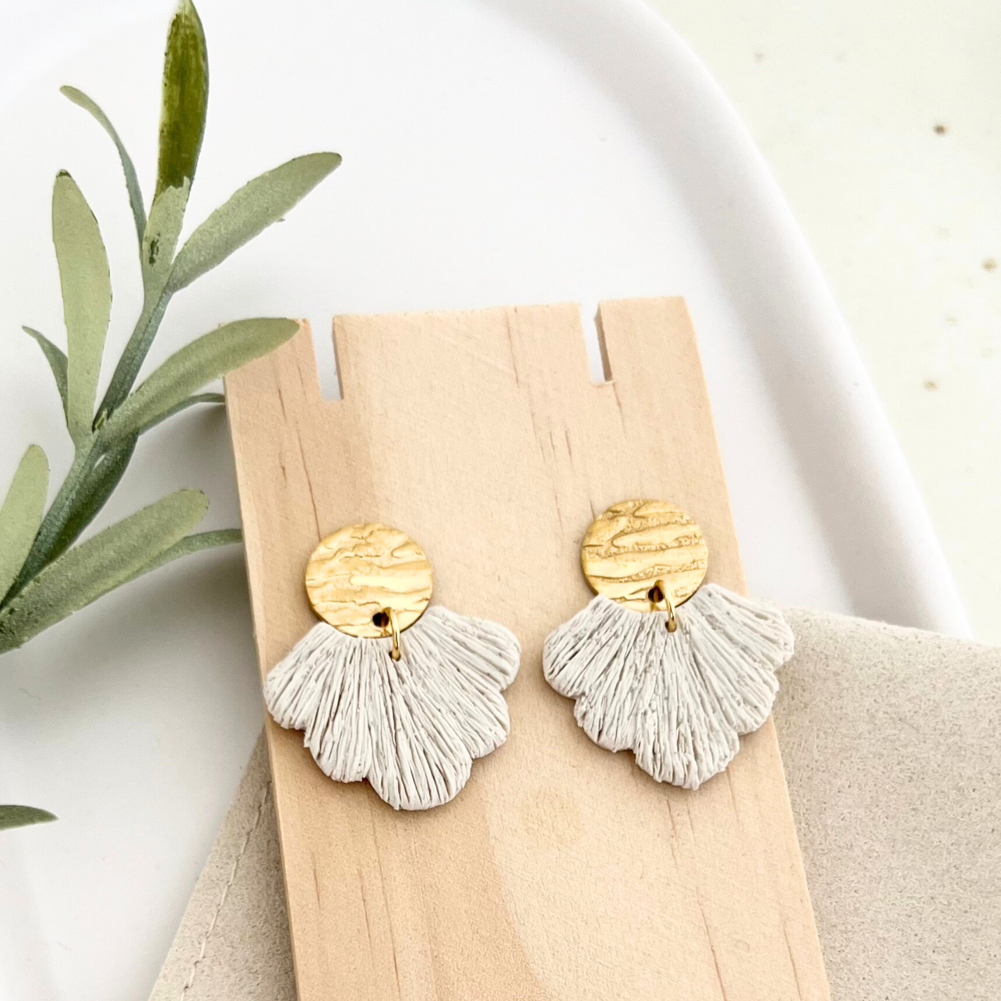 Ohrringe PALERMO im Boho-Stil, goldfarbener Edelstahl mit fächerförmigem Beige-Anhänger aus Polymer Clay, elegant auf Holz präsentiert.