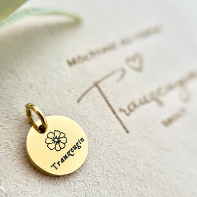 Goldener Anhänger mit der Gravur "Trauzeugin", drapiert auf einer Tasche – symbolisches Geschenk für die Trauzeugin.