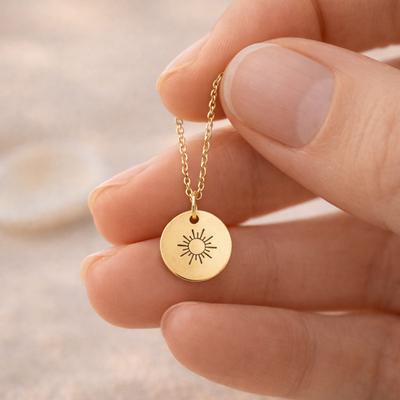 Hand hält eine feine goldene Kette mit rundem Anhänger und Sonnenmotiv, geeignet als persönliches Schmuckstück oder Geschenk mit optionaler Gravur