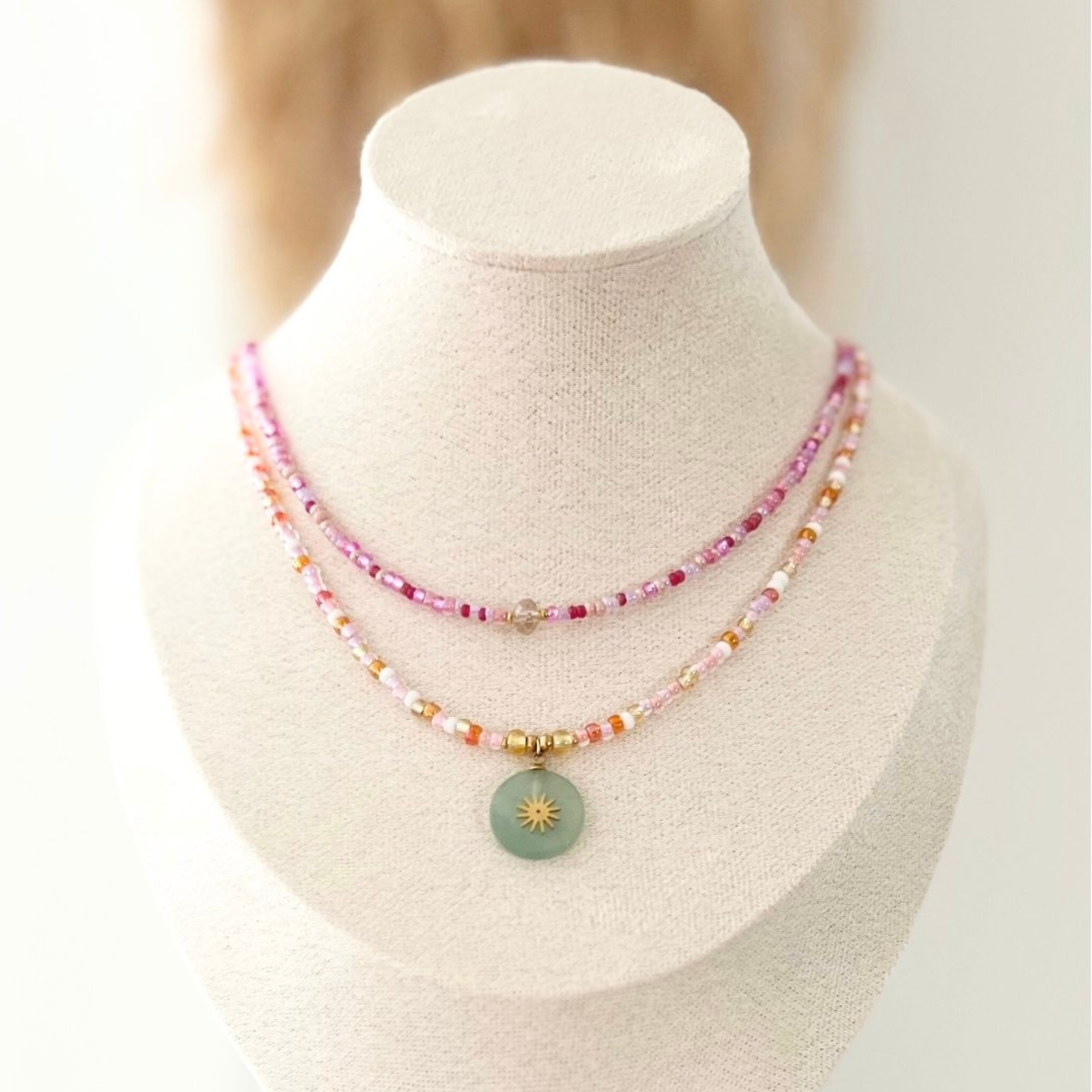 Frontalansicht der Kette ARTÀ mit dem leuchtenden Naturstein-Sonnenanhänger, umrahmt von bunten Rocailles-Glasperlen in Gold, Orange und Pink.
