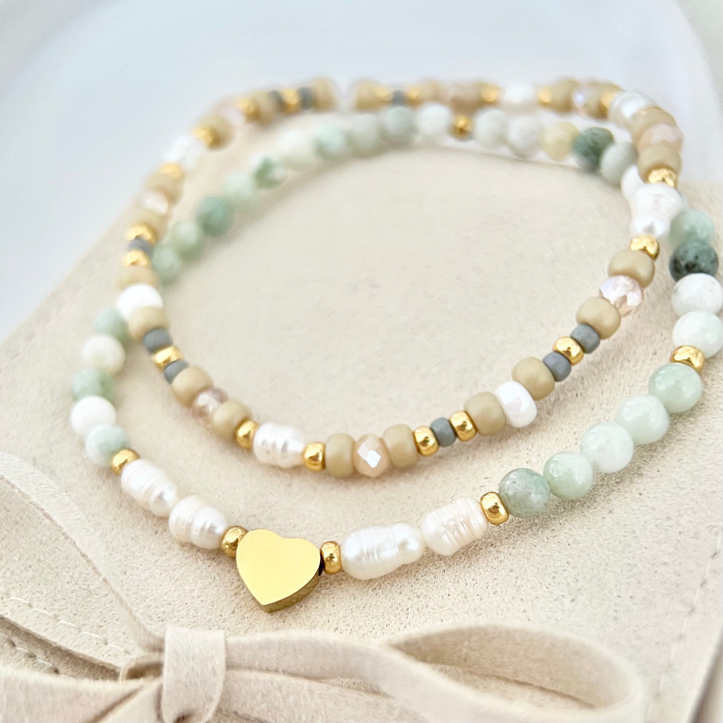 Zwei handgefertigte Armbänder in sanften Grün- und Beigetönen mit goldenen Details, auf einem beigen Schmuckbeutel mit Schleife – Freundschaftsset SOUL, voller Gefühl.