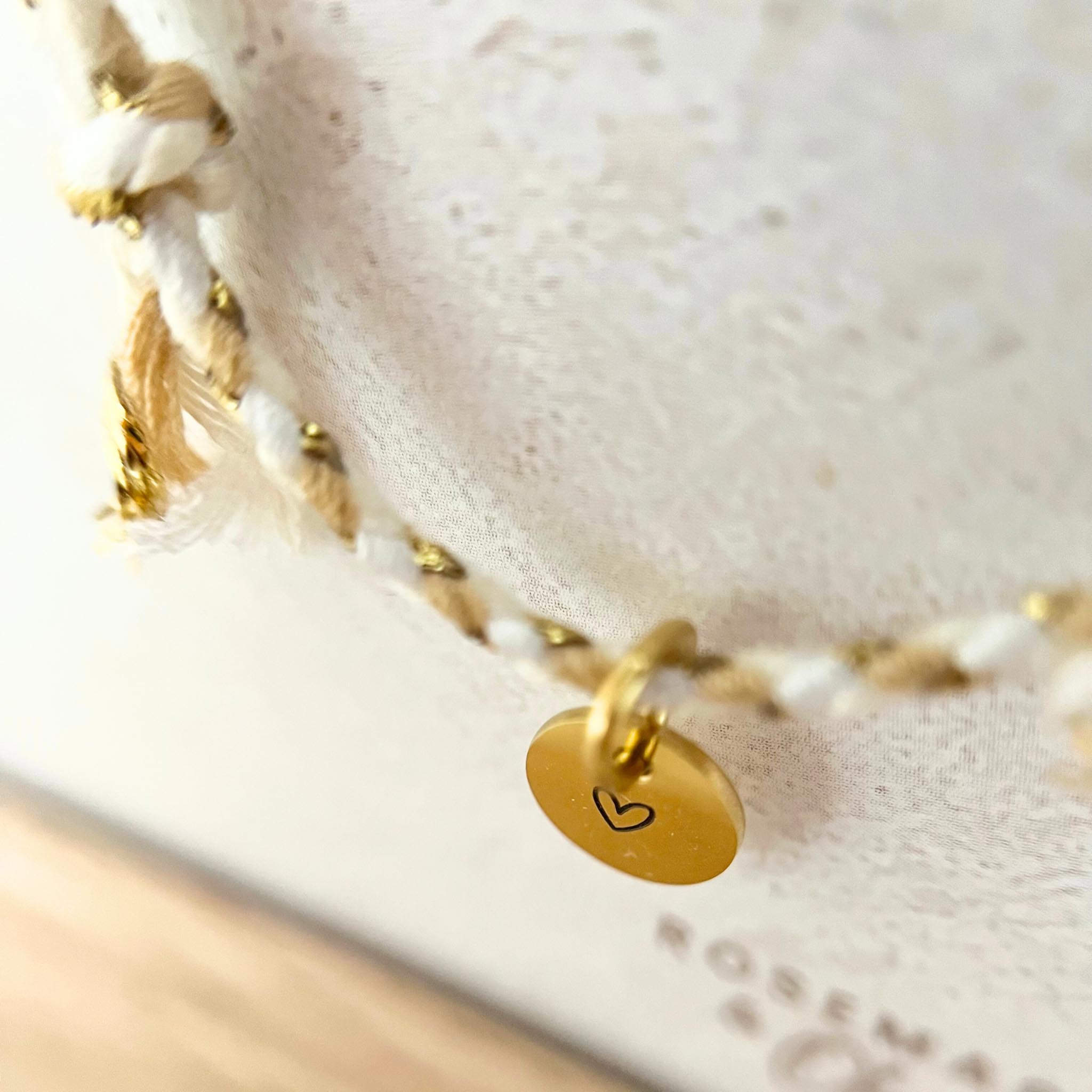 Seitliche Aufnahme des goldfarbenen Anhängers mit Herzgravur auf dem Armband VINYOLA, das zarte Baumwollkordel mit goldenen Akzenten kombiniert