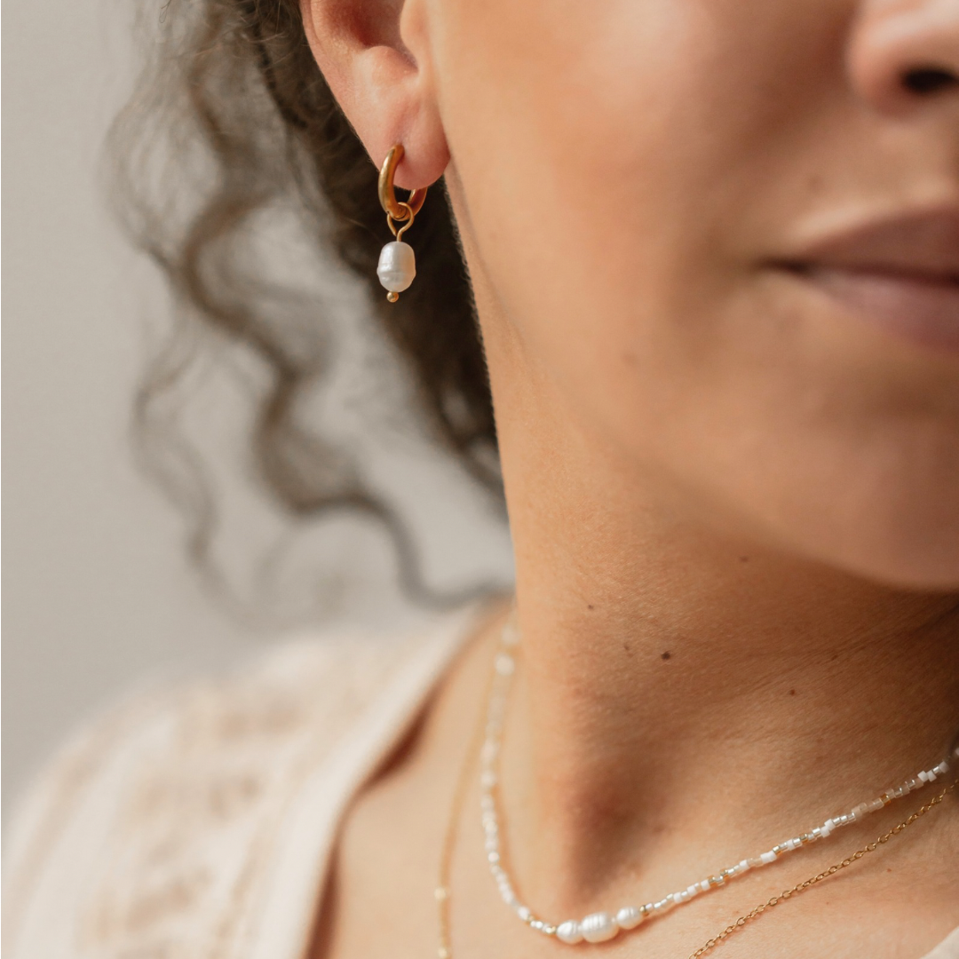 Nahaufnahme eines goldenen Edelstahl-Ohrrings ISLA mit Süßwasserzuchtperle, getragen von einem Model, das den minimalistischen Charme des Designs zeigt.