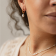 Nahaufnahme eines goldenen Edelstahl-Ohrrings ISLA mit Süßwasserzuchtperle, getragen von einem Model, das den minimalistischen Charme des Designs zeigt.