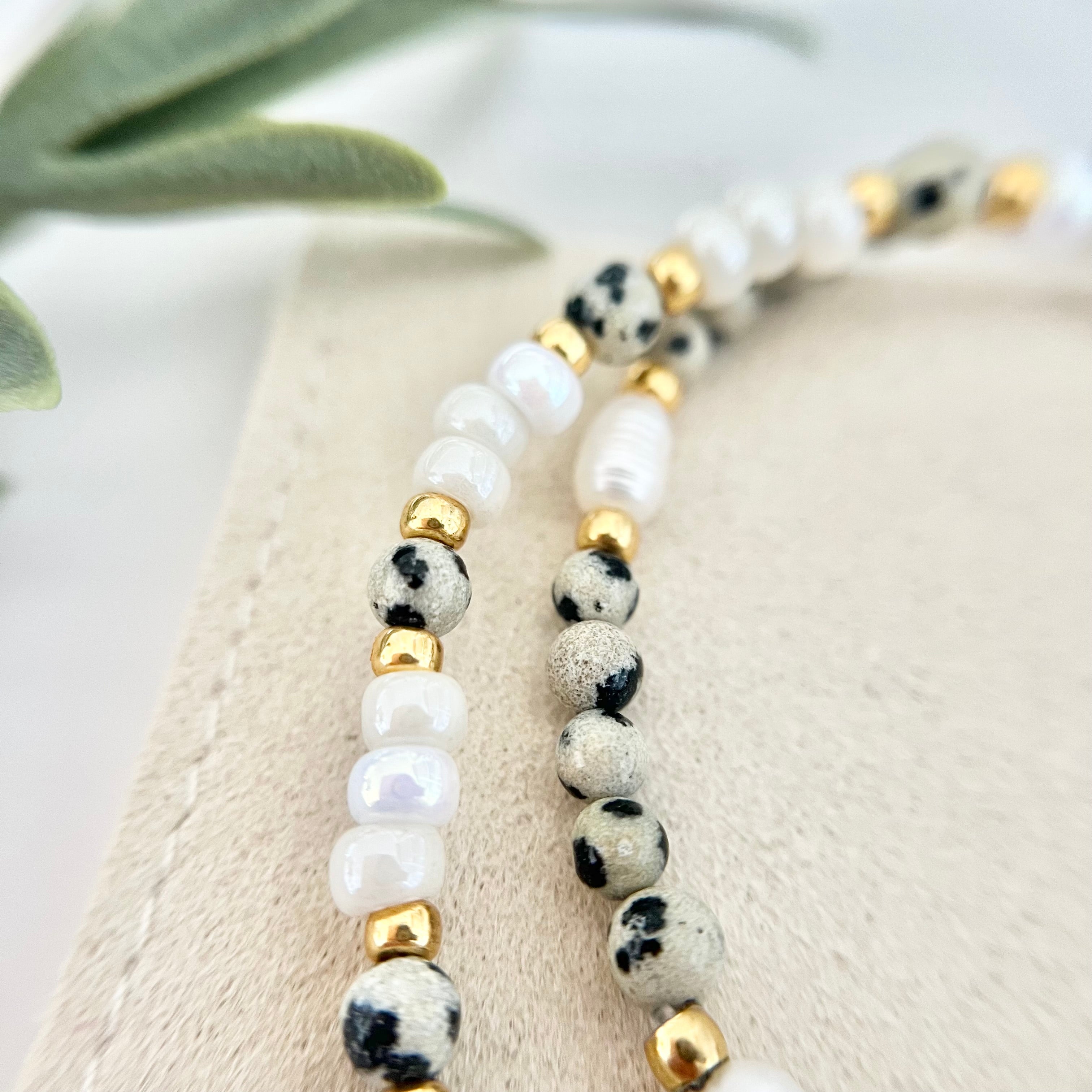 Nahaufnahme zweier Armbänder mit Süßwasser- und Natursteinperlen im Leo-Look, kombiniert mit goldenen Zwischenperlen auf Stoffuntergrund.