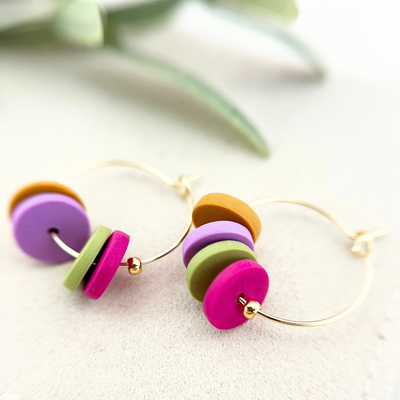 Nahaufnahme der goldfarbenen Creolen HOOPS aus Edelstahl mit zwei bunten Polymer Clay-Anhängern, die perfekt zu Casual- und Party-Looks passen