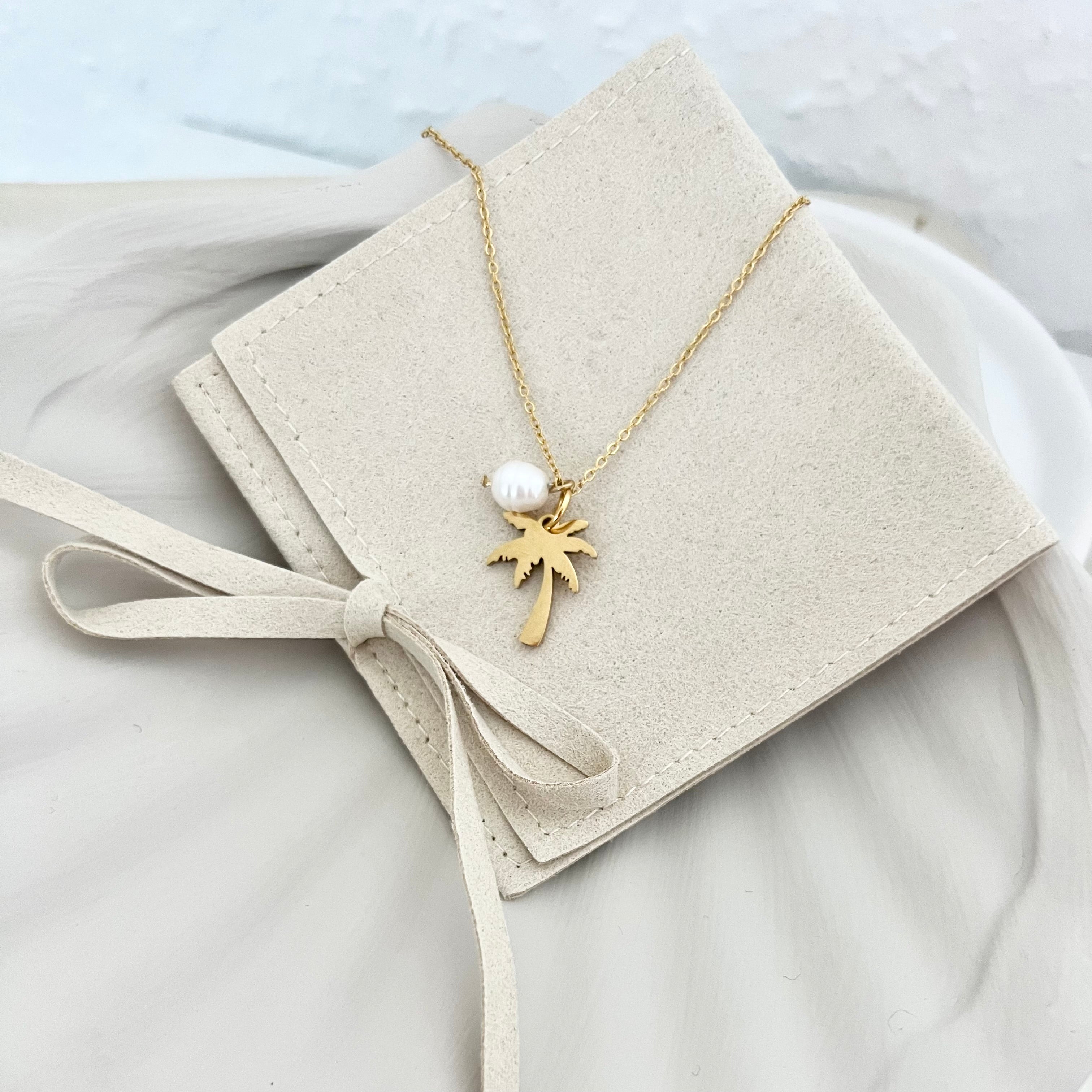 Gesamtansicht der Kette BONITA, die auf einer Tasche drapiert ist, mit Fokus auf den tropischen Palmenanhänger und der stilvollen Süßwasserperle.