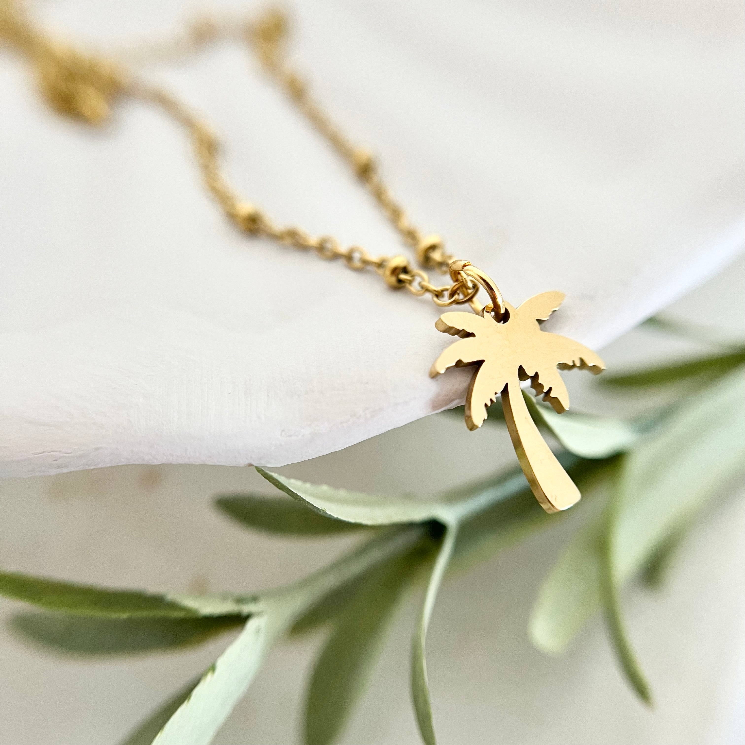Nahaufnahme der Kette PALMERA mit goldenem Palmenanhänger, der tropisches Flair versprüht und für einen stilvollen Sommerlook sorgt.
