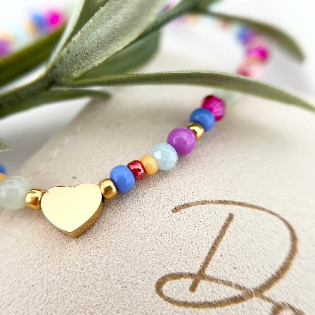 Detailaufnahme eines bunten Armbands aus Glas- und Natursteinperlen mit goldenem Herzanhänger, dekorativ auf Schmuckverpackung mit Schriftzug Danke präsentiert