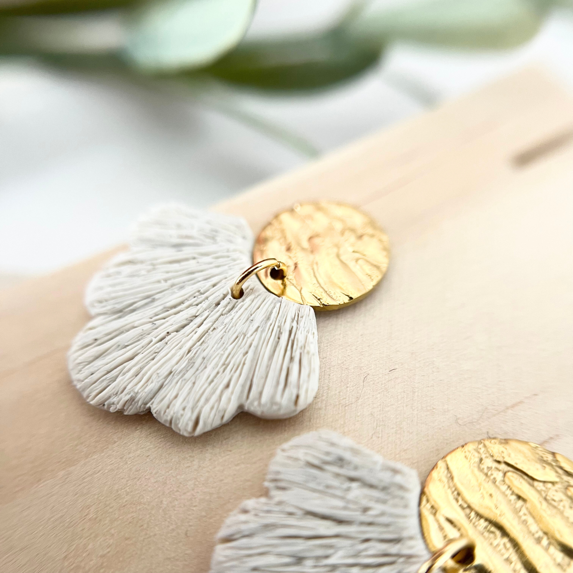 Detailaufnahme der goldfarbenen Ohrringe PALERMO mit fächerförmigem Anhänger aus Polymer Clay, seitlich auf Holz fotografiert.