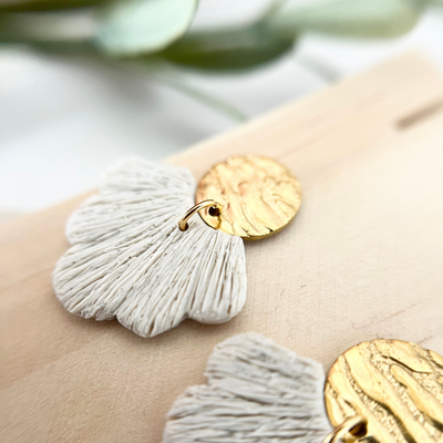 Detailaufnahme der goldfarbenen Ohrringe PALERMO mit fächerförmigem Anhänger aus Polymer Clay, seitlich auf Holz fotografiert.