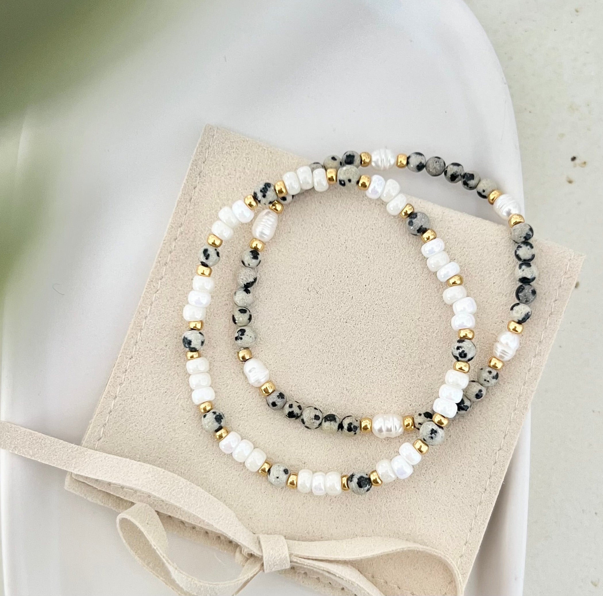 Zwei Armbänder im modernen Leo-Stil auf Schmuckbeutel mit Schleife, Beige- und Weißtöne mit goldenen Akzenten, stilvoll präsentiert.