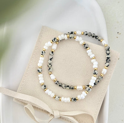 Zwei Armbänder im modernen Leo-Stil auf Schmuckbeutel mit Schleife, Beige- und Weißtöne mit goldenen Akzenten, stilvoll präsentiert.