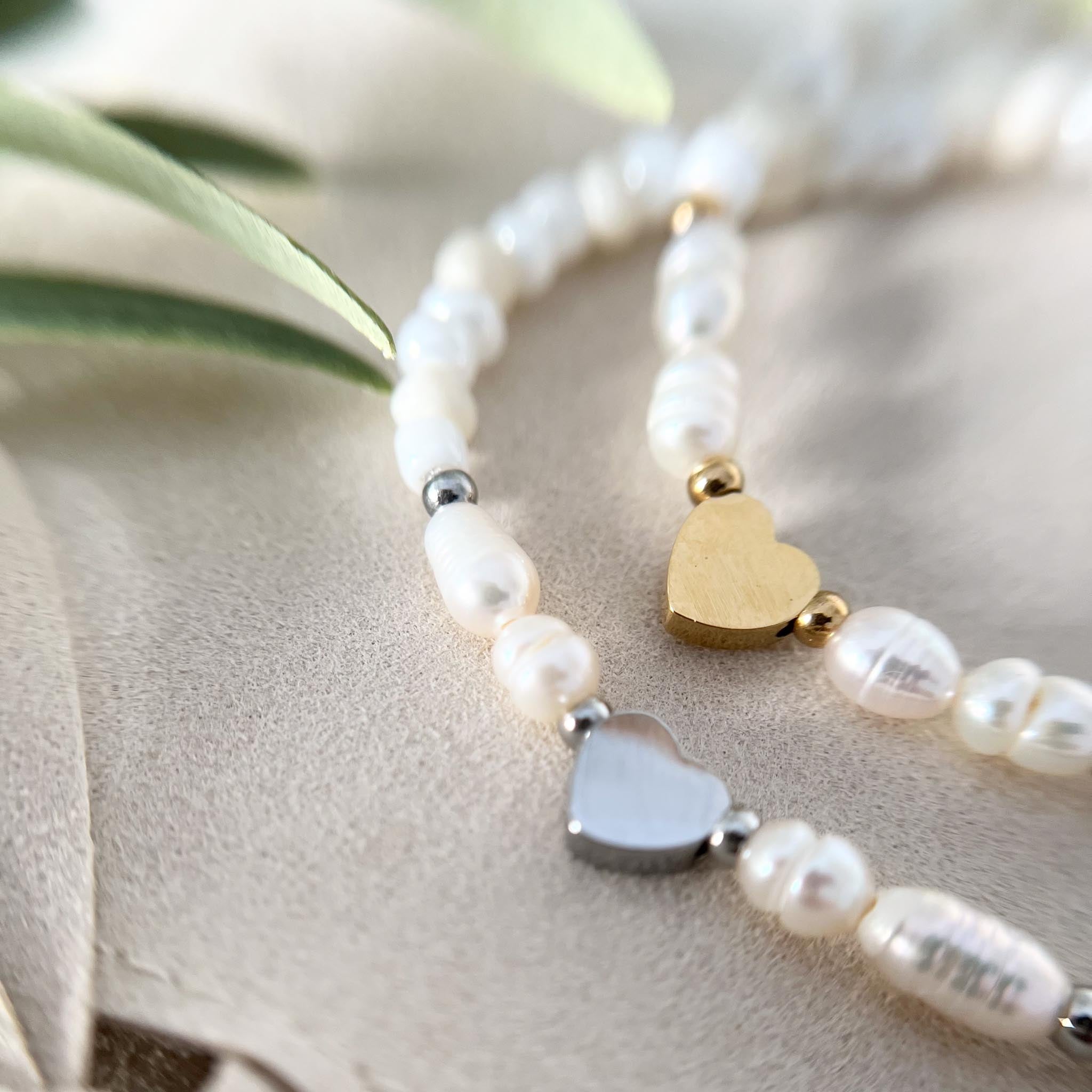 Vergleich von goldfarbenem und silbernem Herzanhänger auf dem Cremeweiß Süßwasserperlen-Armband