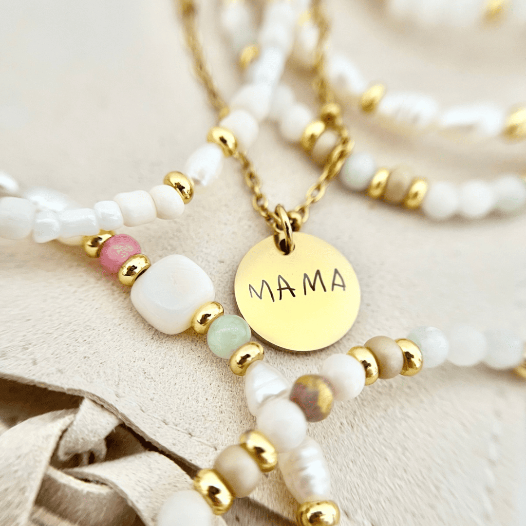 Goldener Anhänger mit der Aufschrift "Mama", umgeben von Perlenketten – Namensanhänger als persönliches Geschenk.