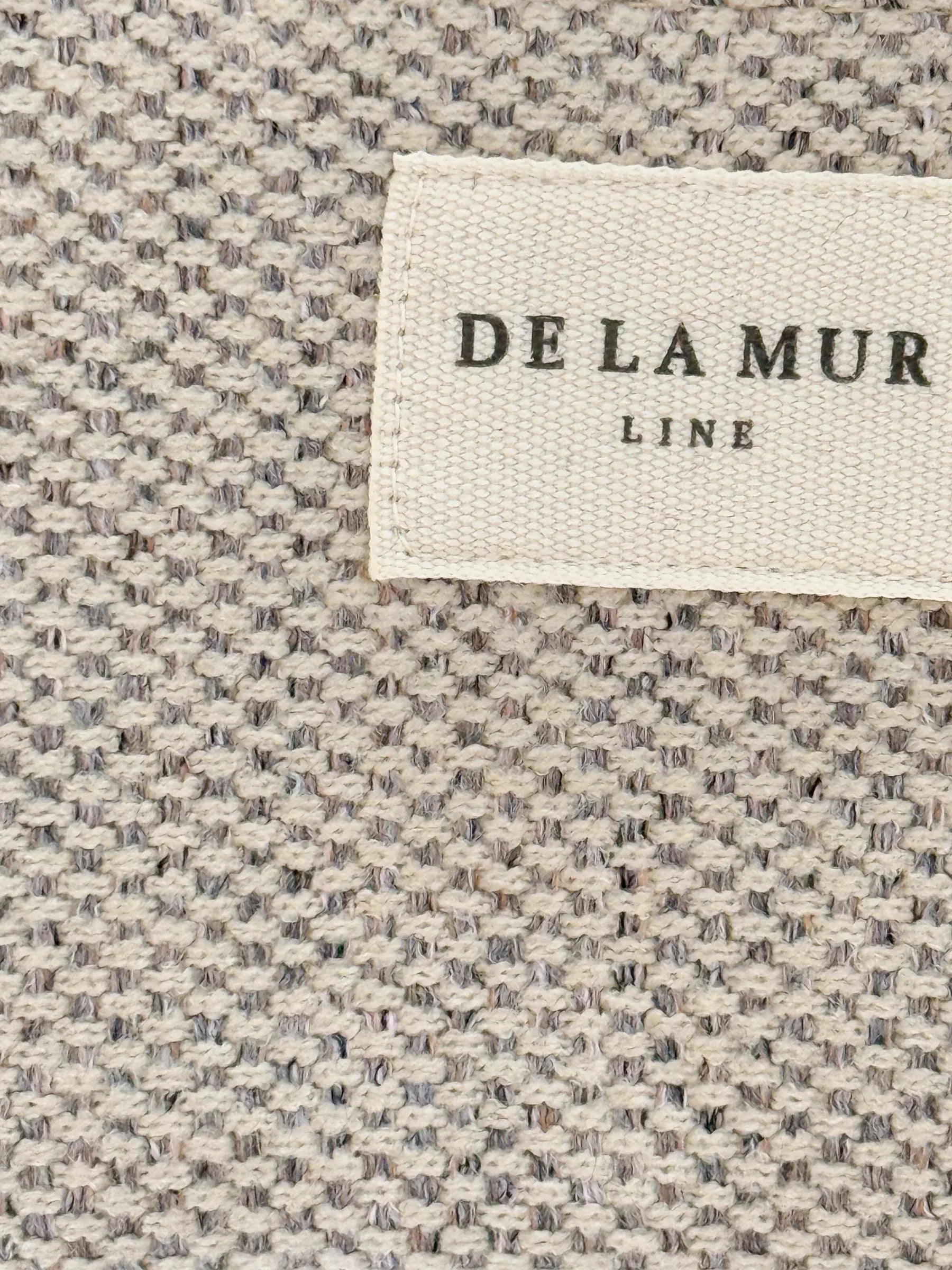 Nahaufnahme des beigen Möbelstoffs mit gewebter Struktur und DE LA MUR Label – handgefertigt in Barcelona.