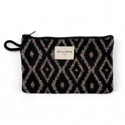 Rechteckige kleine Jacquard-Tasche von DE LA MUR mit grafischem Rautenmuster in Beige auf schwarzem Hintergrund, Reißverschluss und seitlicher Kordelschlaufe. Dient zur Aufbewahrung von Make-up, Pflegeprodukten oder Schmuck.