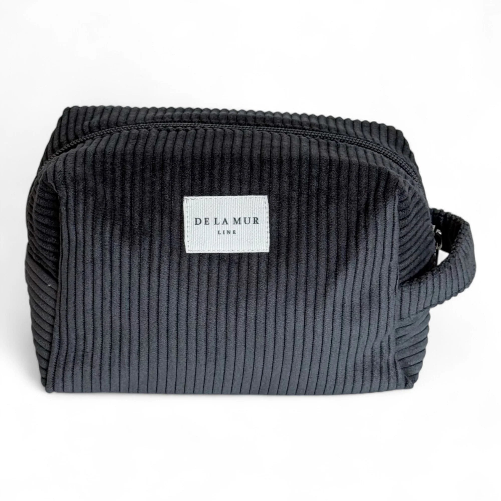 Rechteckige Beauty Bag Medium von DE LA MUR aus anthrazitfarbenem Cordstoff mit feiner Rippenstruktur, Reißverschluss und seitlicher Trageschlaufe. Praktische Kulturtasche zur Aufbewahrung von Kosmetik, Pflegeprodukten oder Schmuck unterwegs.