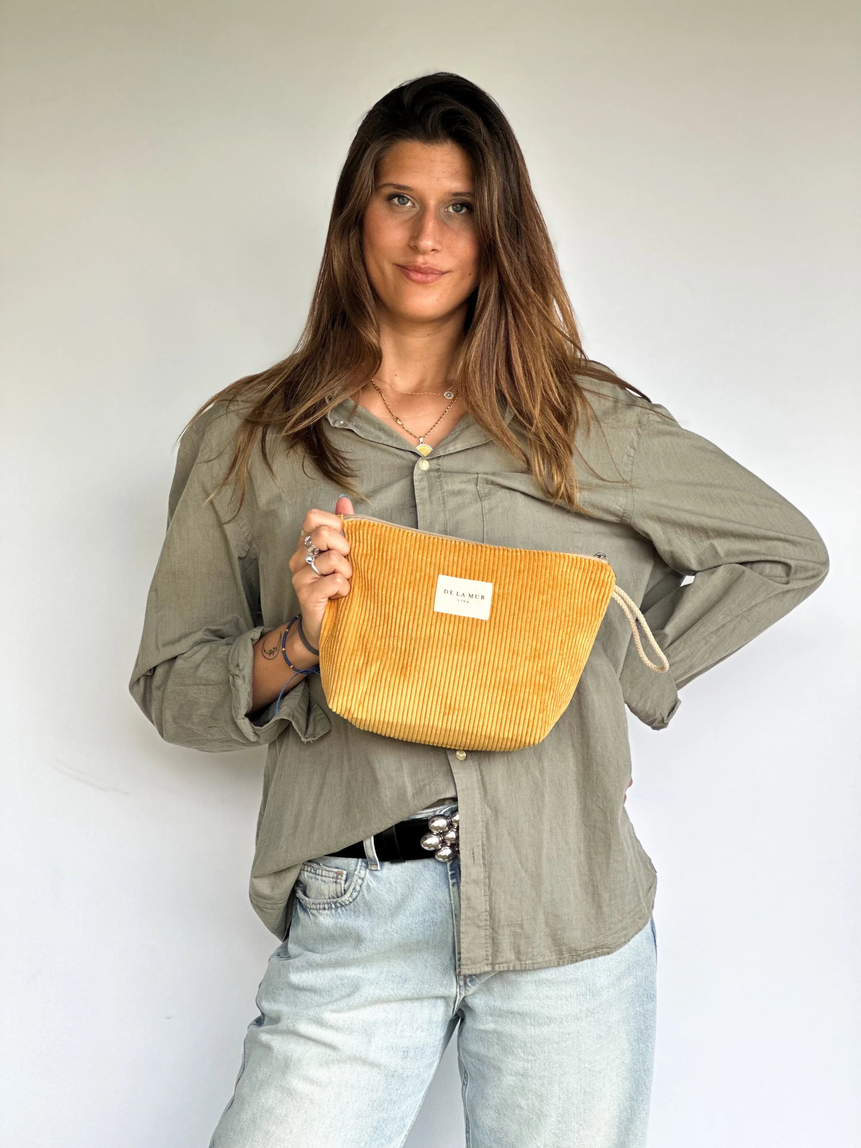Frau hält eine große senfgelbe Beauty Bag von DE LA MUR aus Cordstoff mit Rippenstruktur in den Händen. Handgefertigte Kosmetiktasche zur Aufbewahrung von Pflegeprodukten, Make-up oder Schmuck – inspiriert von warmen Sommertagen und mediterranem Design.