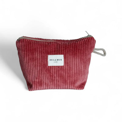 Eine kleine, korallfarbene Cord-Tasche mit sichtbarer Rippenstruktur. Vorne befindet sich ein weißes DE LA MUR Label. Die Tasche steht frei vor weißem Hintergrund, oben ist ein grauer Reißverschluss sichtbar.