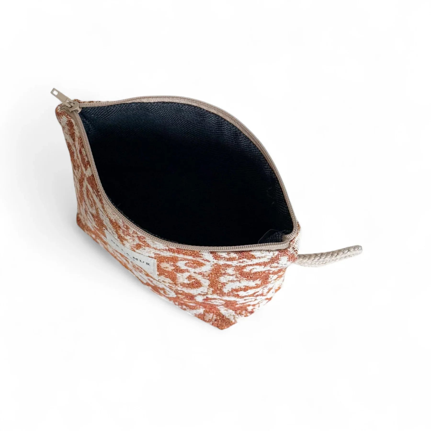 Eine kleine geöffnete Kosmetiktasche aus Jacquardstoff liegt vor weißem Hintergrund. Das Muster ist rostbraun mit hellen Ornamenten, das Innenfutter dunkel. Der Reißverschluss ist geöffnet, an der Seite befindet sich eine kurze Schlaufe.