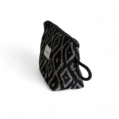 Eine geöffnete Kosmetiktasche mit schwarzem Jacquardstoff und beigefarbenem Diamantmuster liegt vor weißem Hintergrund. Das Innere ist dunkel gefüttert, der Reißverschluss geöffnet, seitlich befindet sich eine kleine Schlaufe.