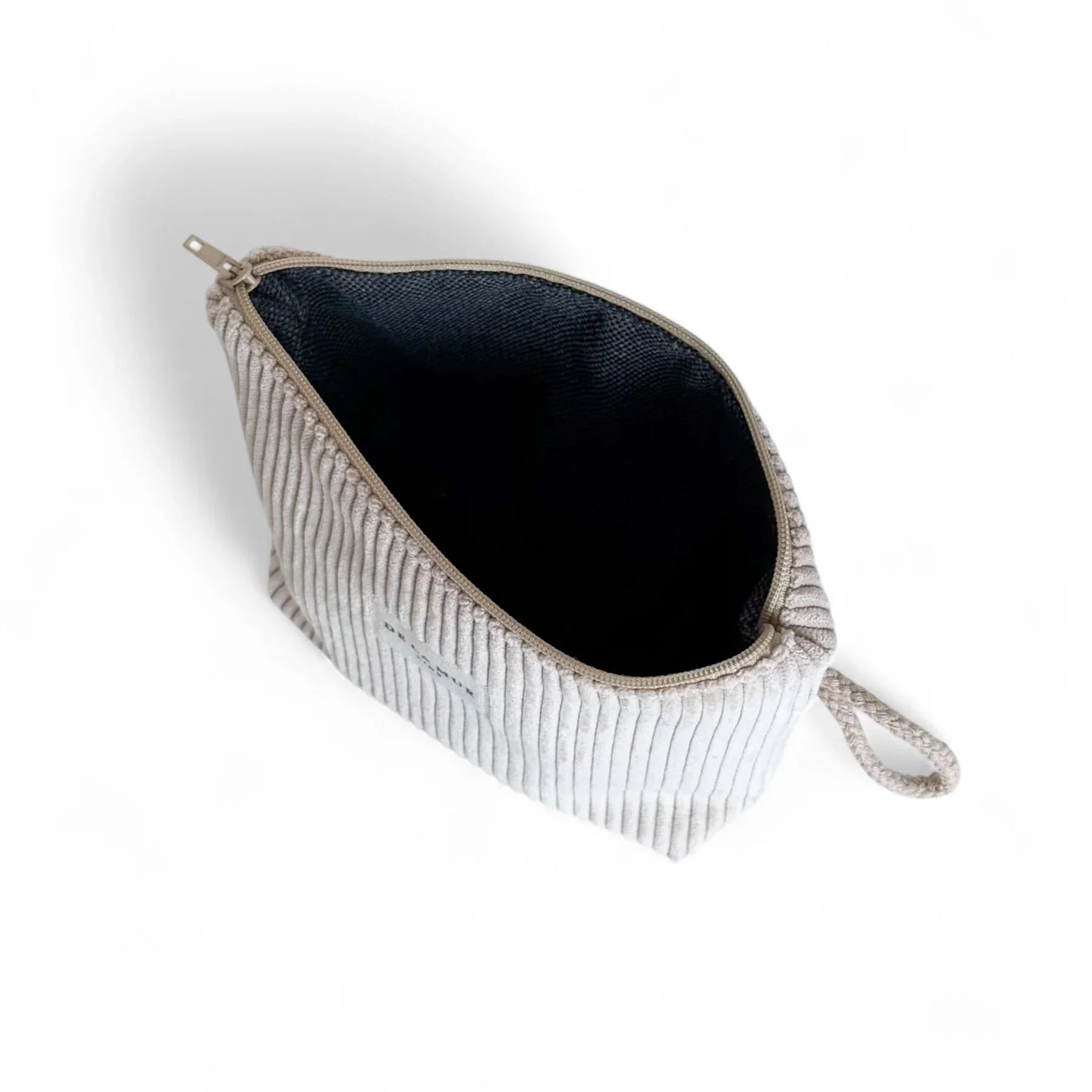 Eine geöffnete, sandfarbene Cord-Tasche mit deutlich sichtbarer Rippenstruktur liegt vor weißem Hintergrund. Der Reißverschluss ist geöffnet, das Innenfutter dunkel, seitlich befindet sich eine kurze Schlaufe.