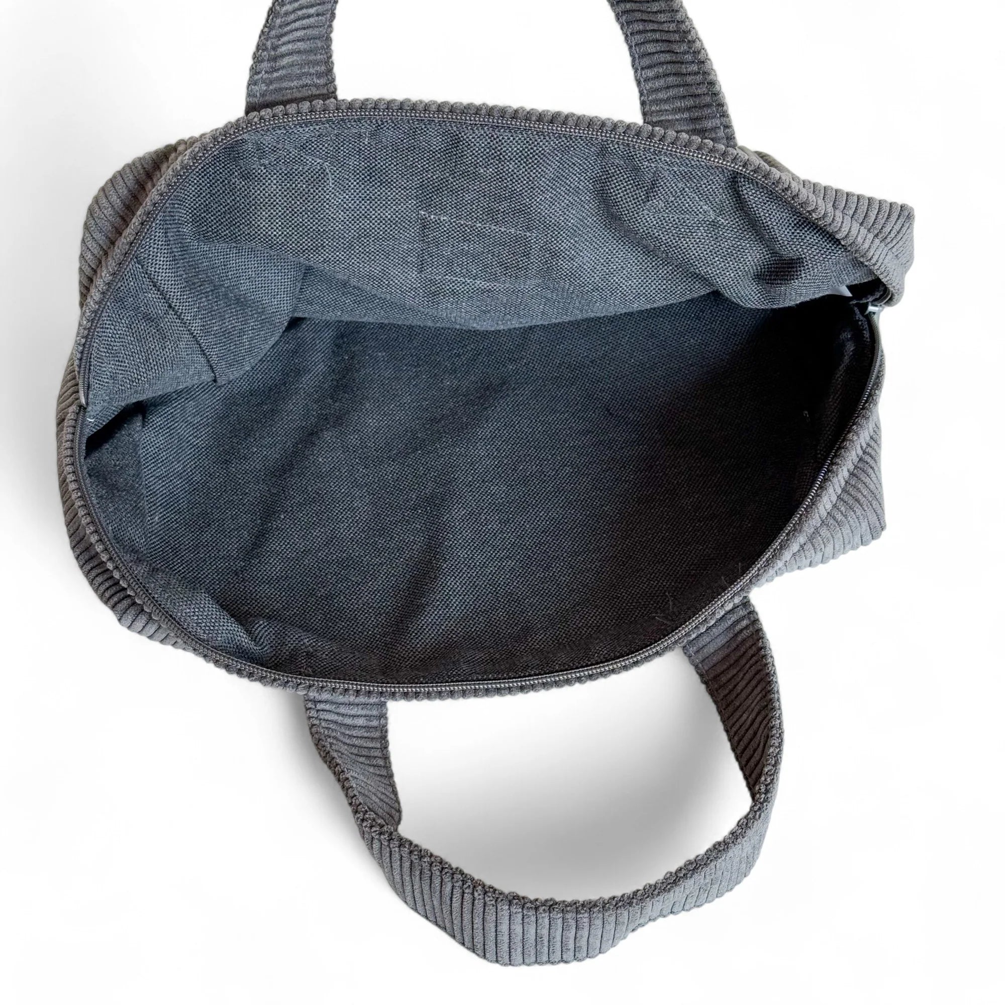 Große, weiche Kosmetiktasche aus dunkelgrauem Cordstoff mit feinen Rippen und zwei Griffen. Auf der Vorderseite ist ein helles Stofflabel mit der Aufschrift „DE LA MUR Line“ zu sehen. Die Tasche ist geöffnet und zeigt ihr dunkles Innenfutter.