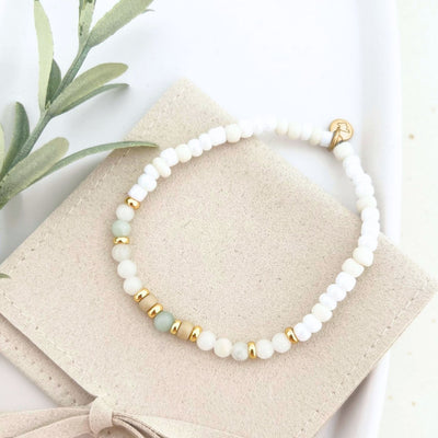 Vollansicht des Armbands BELLINI in einer eleganten Tasche, mit einem goldenen Gravur-Anhänger und Natursteinperlen als Glücksbringer