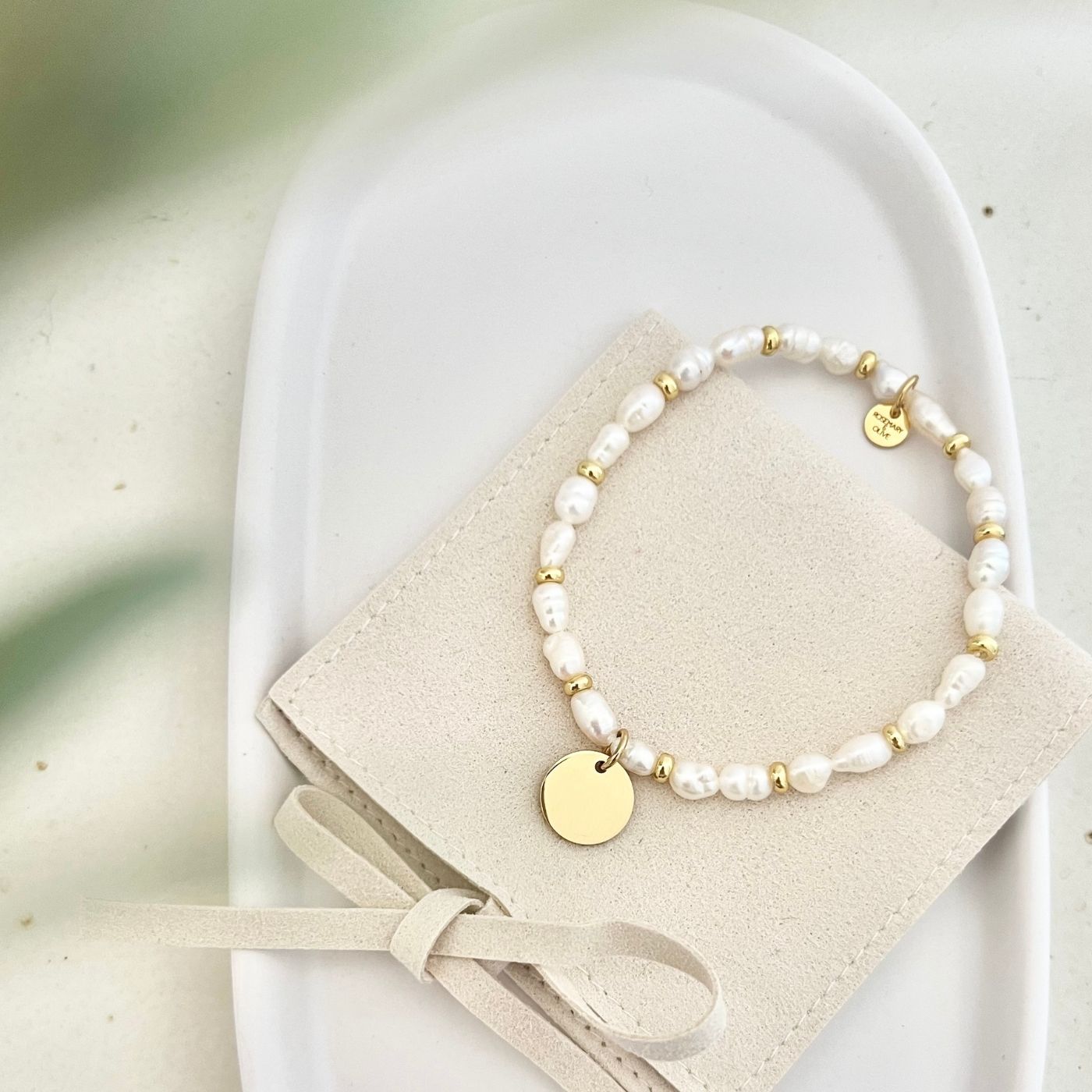 Vollansicht des handgemachten Armbands ALVA mit goldfarbenem Edelstahl-Anhänger und Süßwasserperlen, präsentiert in einer eleganten Tasche