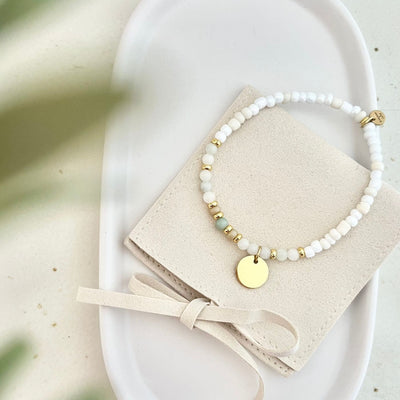 Gesamtansicht des Armbands BELLINI liegend auf einer Tasche – Perlenarmband mit Aventurin Perle in der Mitte und Gravur Anhänger, Symbol für Harmonie und Glück