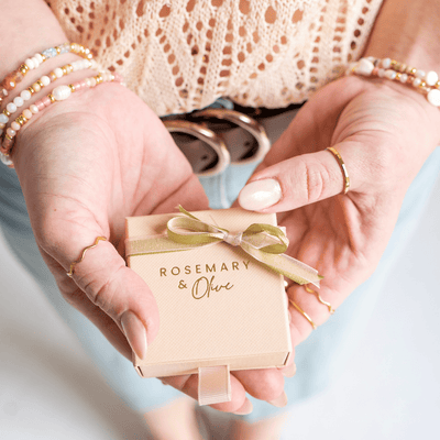 Die Verpackung von Rosemary & Olive wird in zwei Händen gehalten, bereit, die Schmuck zu verschenken oder zu versenden.