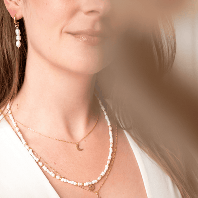 Goldener Edelstahl-Ohrring PERLA mit weißer Süßwasserperle, getragen von einem Model, das den klassischen, vielseitigen Look des Schmuckstücks zeigt.